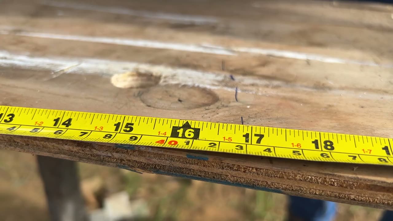 Una mano con guante marca 16 pulgadas en una hoja de plywood, junto a una cinta métrica